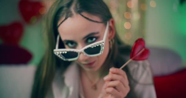 Retrato de close-up de mulher atraente em óculos de sol na moda segurando coração em forma de doce vermelho - Filmagem, Vídeo