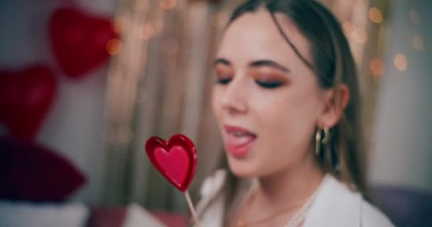 Κοντινό πλάνο της ελκυστική νεαρή γυναίκα γλείφει καραμέλα σχήμα καρδιάς κατά τη διάρκεια της ημέρας Galentines - Πλάνα, βίντεο