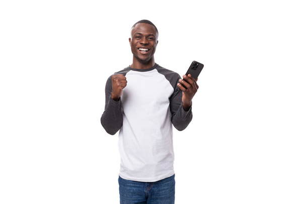 portrét mladého afrického muže s krátkým účesem neformálně oblečeného a držícího v ruce smartphone. - Fotografie, Obrázek