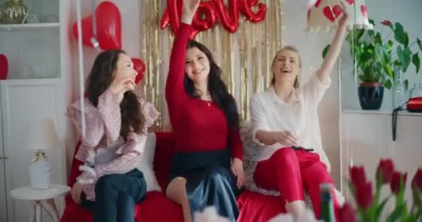 Speelse jonge vrouwelijke vrienden gooien hartvormige ballonnen thuis op Galentines dag - Video