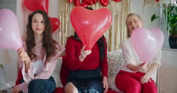 Ευτυχισμένες νεαρές φίλες που κρατούν μπαλόνια σε σχήμα καρδιάς διασκεδάζοντας στο σπίτι την ημέρα του Galentines - Πλάνα, βίντεο