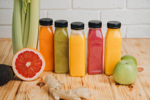 Obst- und Gemüse-Smoothies in transparenten Plastikflaschen. Rote, grüne, orangefarbene Smoothies auf einem Holztisch. Das Konzept der gesunden Ernährung. Frontansicht - Foto, Bild