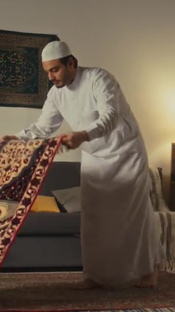 Plně vertikální záběry bosého arabského muslima v čepici a bílé kandoře šířící modlitební rohožku a začínající domácí salát - Záběry, video