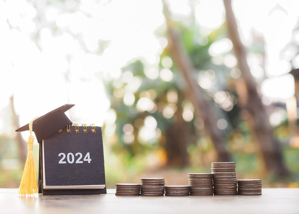 Study goals, 2024 Desk calendar with graduation hat and stack of coins. The concept of saving money for education, student loan, scholarship, tuition fees and manage time to success graduate. - Photo, Image