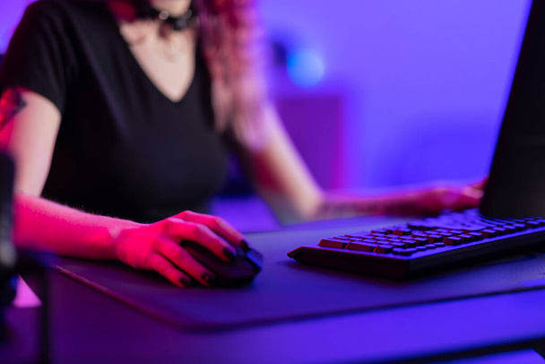 A professional gamer is intensely engaged in an online game, showcased by the vivid glow of a colorful gaming room setup with modern gaming equipment. - Photo, Image