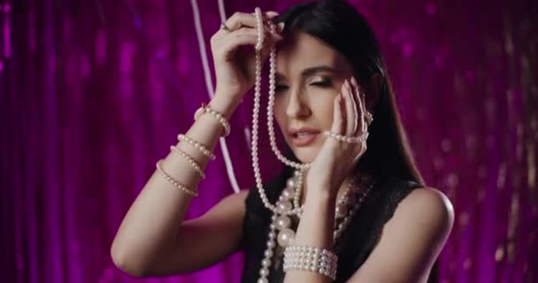 Retrato de mujer joven seductora de moda sosteniendo collar de perlas en frente de la decoración - Metraje, vídeo