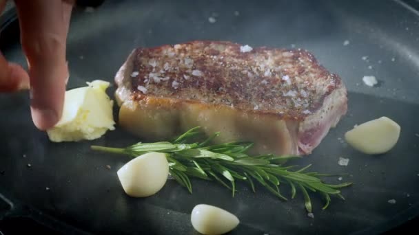 Steak sur une poêle en fonte avec ail et romarin. Préparation des aliments. Vidéo au ralenti, 100 ips. Images 4k de haute qualité. Images 4k de haute qualité - Séquence, vidéo