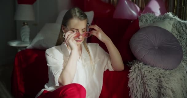 Atrakcyjna młoda kobieta w okularach przeciwsłonecznych pachnąca świeżą czerwoną truskawką opierając się na sofie w domu - Materiał filmowy, wideo