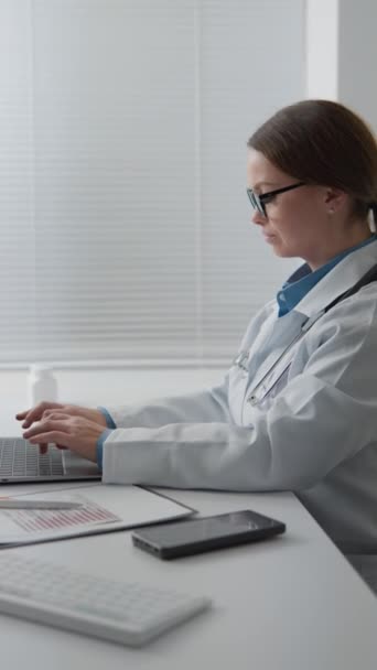 Ein Facharzt mit Stethoskop nutzt effektiv einen Laptop, um medizinische Daten des Patienten zu konsultieren und aufzuzeichnen. Facharzt und medizinischer Experte auf dem Gebiet der Medizin und Behandlung. Hoch - Filmmaterial, Video