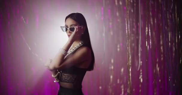Чувственная модная молодая женщина в жемчужных украшениях и солнцезащитных очках на фоне яркого фона - Кадры, видео