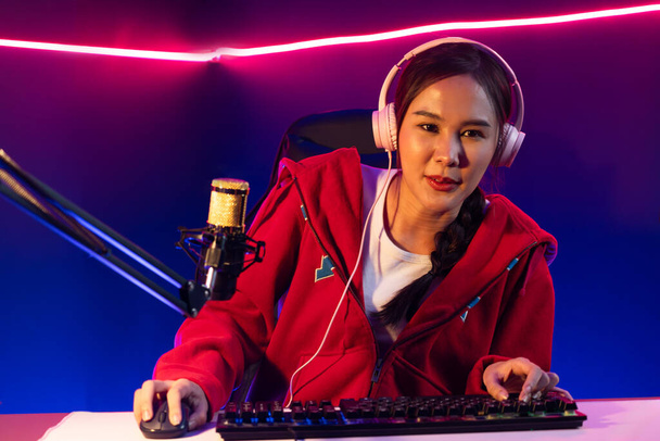 Host channel of smiling beautiful Asian girl streamer playing online game wearing headphone talking with viewers media online recording phone. Esport skilled team players in neon blue room. Stratagem. - Foto, Imagen