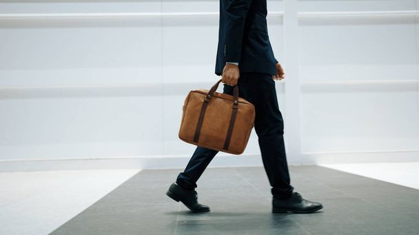 Zbliżenie profesjonalnego biznesmena chodzącego nogą podczas trzymania torby. Przycięty obraz kierownika projektu skupia się na nodze. Podróżowanie, poruszanie się, podróż, chodzenie, zdobywanie nowej pozycji, zmiana pracy. Ekstrakt. - Zdjęcie, obraz