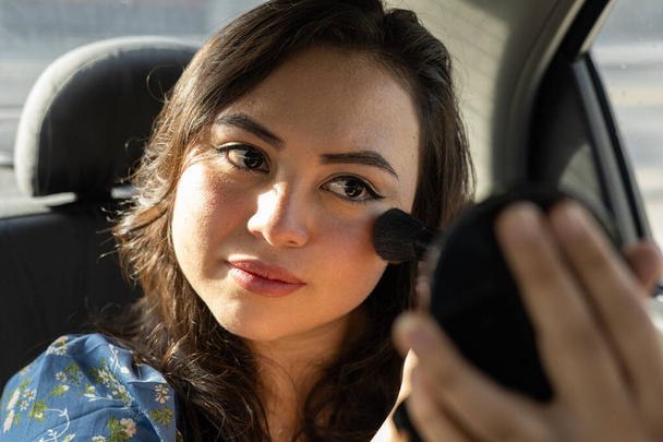 Kısa saçlı, genç bir Latin kadının makyaj rutini. Bir arabanın içinde güne hazırlanan kişinin yaşam tarzı. - Fotoğraf, Görsel