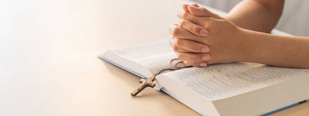 Asian male folded hand prayed on holy bible book while holding up a pendant crucifix. Spiritual, religion, faith, worship, christian and blessing of god concept. Blurring background. Burgeoning. - Photo, Image