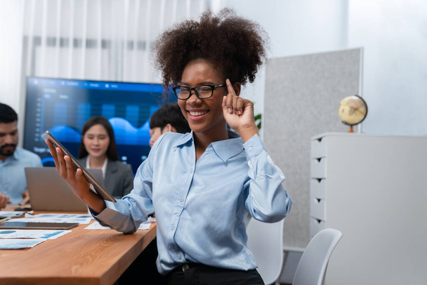 Gelukkige jonge Afrikaanse zakenvrouw draagt een bril portret met een groep kantoormedewerkers op een ontmoeting met scherm display business dashboard op de achtergrond. Zelfverzekerde kantoordame bij de teamvergadering. Koord - Foto, afbeelding