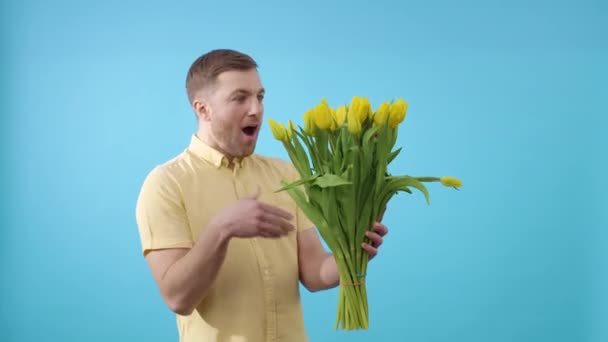 Mann umarmt Bündel gelber Tulpen auf blauem Hintergrund - Filmmaterial, Video