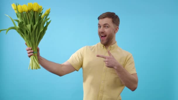 Férfi bemutató csomó sárga tulipán előtt kék háttér - Felvétel, videó