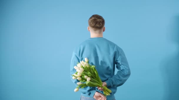 Sonriente hombre se da la vuelta y da un ramo de tulipanes blancos sobre fondo azul - Imágenes, Vídeo