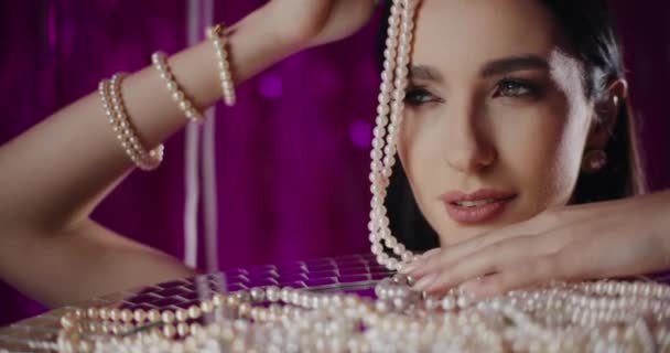 Крупный план замедленной съемки чувственной молодой женщины с жемчужным ожерельем, опирающейся на стеклянный стол - Кадры, видео
