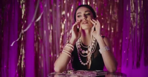 Sensual mujer joven con collar de perlas apoyado en la mesa de cristal en frente de la decoración - Metraje, vídeo