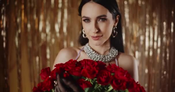 Portret uśmiechniętej atrakcyjnej młodej kobiety trzymającej kilka świeżych róż przed dekoracją - Materiał filmowy, wideo