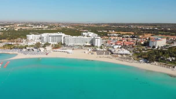 Ayia Napa, Cyprus - 15th april, 2023: Luxury hotel buildings with pools by beach with island greenery panorama. Vehicles in Nissi bay parking. - Footage, Video