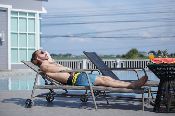 Kaukázusi jóképű férfi napszemüvegben fekszik a medence mellett, hétvégi pihenés luxus utazási medence mellett. Nyári szabadság koncepciója. - Fotó, kép