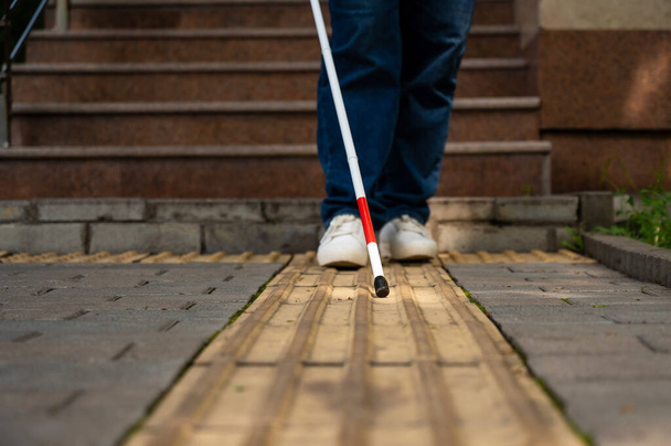 A blind woman walks outdoors using a cane along a tactile yellow tile - Fotoğraf, Görsel