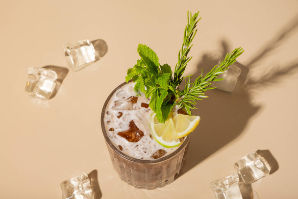Decoración de cóctel alcohólico menta, limón y cubos de hielo sobre una vista superior de fondo beige, plano. - Foto, Imagen