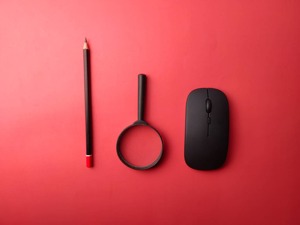 Disposizione vista dall'alto mouse wireless, matita e lente d'ingrandimento su sfondo rosso - Foto, immagini