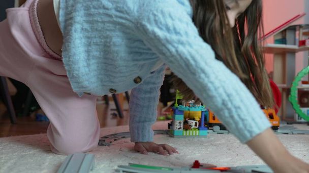 Een klein meisje dat met treinspeelgoed speelt op de vloer. 8 jaar oud kind verdiept in het spel met rails en speelgoed - Foto, afbeelding