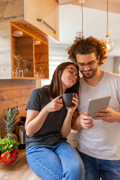 Couple in love drinking coffee and surfing the Internet using a tablet computer in the kitchen - Photo, image