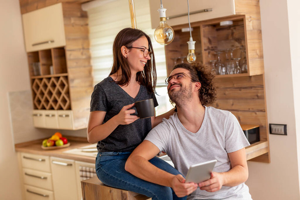 Young couple in love drinking coffee and using a tablet computer in the kitchen - 写真・画像