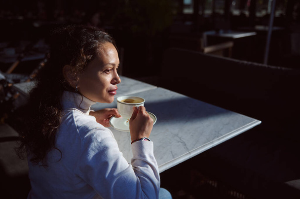 Magabiztos és vonzó göndör hajú fiatal nő félrenéz, miközben a kávézóban ül, és élvezi a kávészünetét. Emberek! Élelmiszer - és italfogyasztás fogalma - Fotó, kép