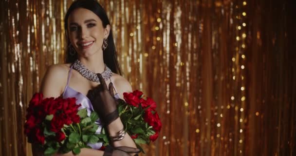 Sorrindo atraente jovem segurando rosas vermelhas contra decoração streamer - Filmagem, Vídeo