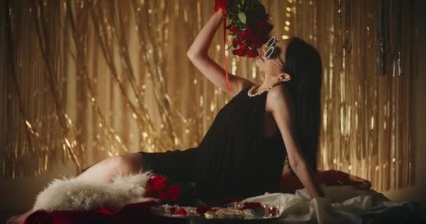 Mosolygó érzéki fiatal nő gyöngyszemüveg kezében rózsa, miközben feküdt az ágyon megvilágított hálószobában - Felvétel, videó