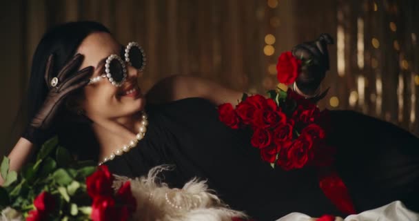 Χαμογελώντας αισθησιακή νεαρή γυναίκα σε μαργαριταρένια γυαλιά μυρίζοντας φρέσκο τριαντάφυλλο, ενώ βρίσκεται στο κρεβάτι - Πλάνα, βίντεο