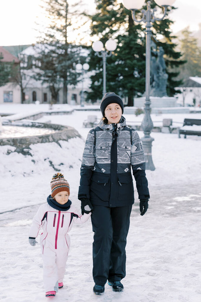 Äiti ja pikkutyttö kävelevät käsi kädessä lumisessa puistossa. Laadukas kuva - Valokuva, kuva