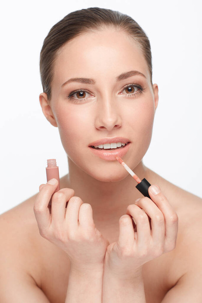 Woman, face and lipstick or makeup and beauty with gloss, shine and cosmetology on white background. Hands, portrait and cosmetic product for lips, change or transformation in studio with wellness. - Photo, image