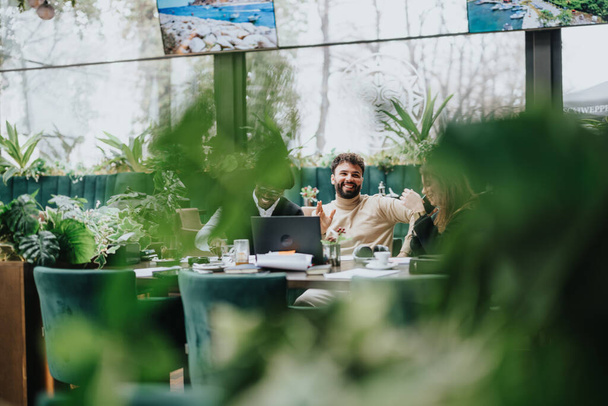 Multiethnic professionals working together, using a laptop in a plant-filled restaurant. A feeling of collaboration and camaraderie is present. - Photo, Image