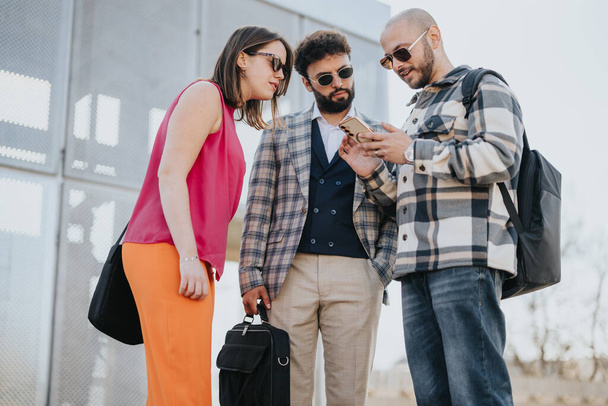 Три молодых профессионала ведут деловую беседу на открытом воздухе в центре города, рассматривая контент на смартфоне. - Фото, изображение