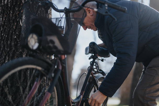 Старший чоловік в зимовій куртці, що виконує обслуговування на велосипеді на відкритому повітрі. - Фото, зображення