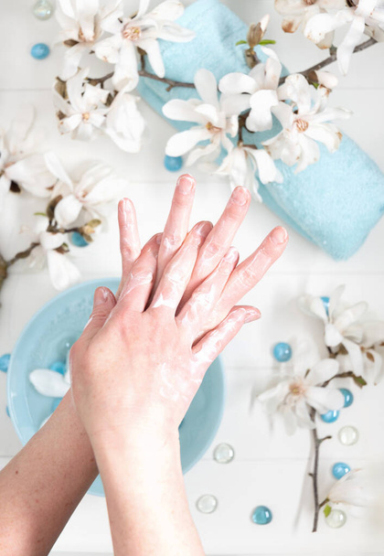νεαρή γυναίκα κάνει βήμα προς βήμα μασάζ δάχτυλο με κρέμα στο σαλόνι με φλιτζάνι νερό πηγής και μπλε πέτρες spa και λευκά λουλούδια μανόλια, υψηλής ποιότητας φωτογραφία - Φωτογραφία, εικόνα