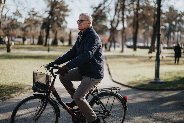 Uomo anziano attivo che si gode un giro in bicicletta nel parco soleggiato concetto di stile di vita sano. - Foto, immagini