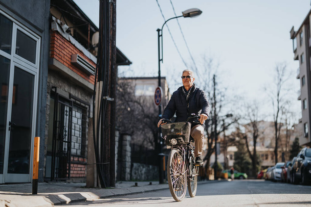 静かな住宅街道を自信を持ってサイクリングするアクティブな高齢者,晴れた日の暖かい輝きをベースに. - 写真・画像