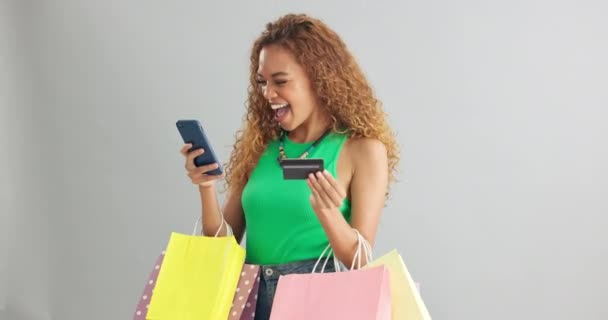 Happy woman, phone and credit card with shopping bags for payment on a gray studio background. Female person with smile or debit on mobile smartphone for online purchase, banking or app on mockup. - Felvétel, videó