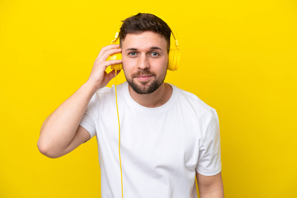 Junger kaukasischer Mann isoliert auf gelbem Hintergrund Musik hörend - Foto, Bild
