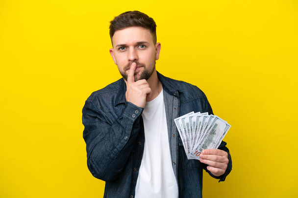 Jeune homme caucasien prenant beaucoup d'argent isolé sur fond jaune ayant des doutes tout en levant les yeux - Photo, image