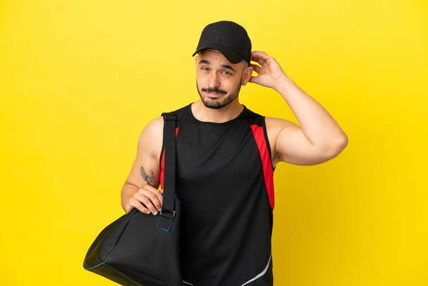 Young sport caucasian man with sport bag isolated on yellow background having doubts - Photo, Image