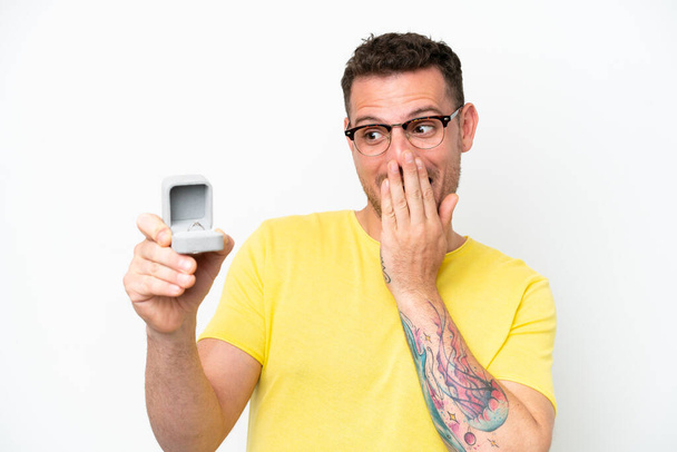 Young caucasian man holding a engagement ring isolated on white background with surprise and shocked facial expression - Foto, immagini